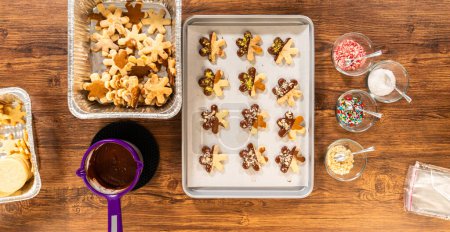 Téléchargez les photos : Fabrication de biscuits de vacances en forme d'étoile trempés dans du chocolat et saupoudrés de pistaches concassées, disposés sur du papier parchemin. - en image libre de droit