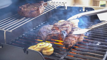 Photo for The outdoor two-burner gas grill is put to good use, sizzling with the sound and aroma of ribeye steaks and onion rings being perfectly cooked. - Royalty Free Image