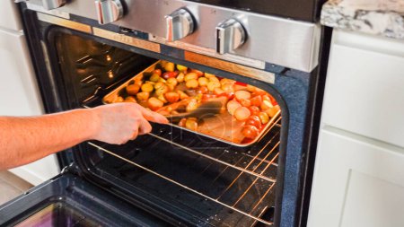 Photo for Within the setting of a modern kitchen, a young man is immersed in preparing dinner, currently roasting seasoned rainbow potatoes in the oven, an important step towards a delightful meal. - Royalty Free Image