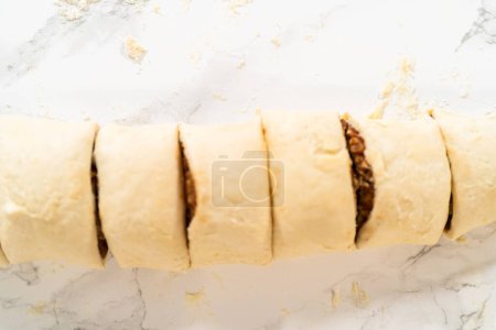 Téléchargez les photos : Coupe de pâte à pain roulée remplie de cannelle et de pacanes hachées en petits rouleaux pour cuire des cupcakes à la cannelle sans levure. - en image libre de droit