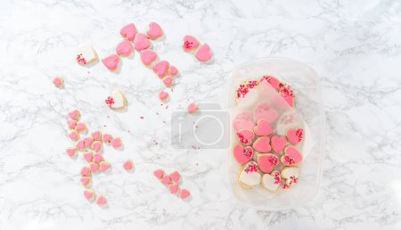 Photo for Flat lay. Storing heart-shaped sugar cookies with pink and white royal icing in a large plastic container. - Royalty Free Image
