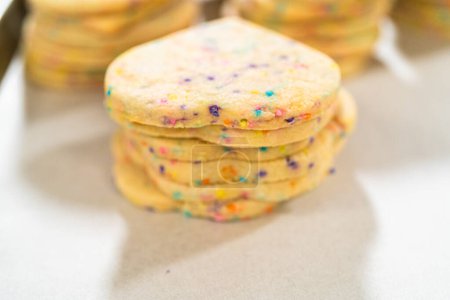 Photo for Large quantity of sprinkle-filled sugar cookies are neatly stacked on a baking tray, awaiting their packaging into the rustic brown paper boxes. - Royalty Free Image
