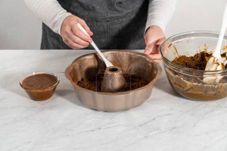 Téléchargez les photos : Remplissage casserole de gâteau bundt en métal avec du beurre de gâteau pour cuire le gâteau bundt en pain d'épice avec remplissage au caramel. - en image libre de droit