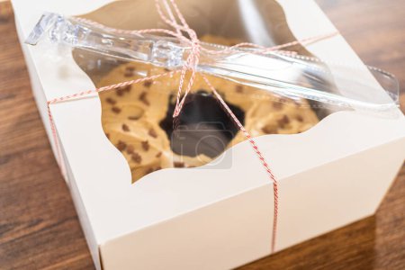 Foto de Colocar cuidadosamente el pastel de pan de jengibre, adornado con glaseado de caramelo salado y aspersiones de pan de jengibre, en una caja de pastel de paquete de papel blanco con una ventana transparente para regalar. - Imagen libre de derechos