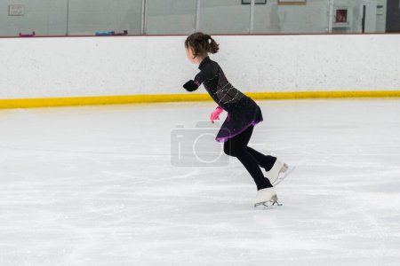 Foto de Jovencita perfeccionando su rutina de patinaje artístico mientras usa su vestido de competición en una pista de hielo interior. - Imagen libre de derechos