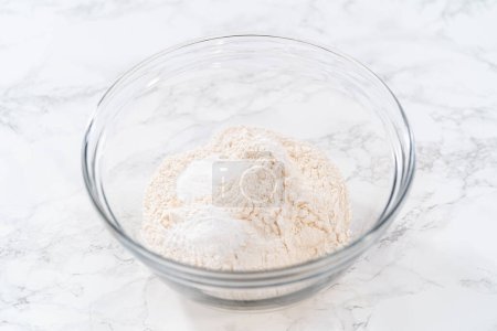 Foto de Mezclar ingredientes secos con un batidor de mano en un tazón de vidrio para hornear magdalenas de semillas de amapola de limón. - Imagen libre de derechos