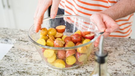 Photo for In a sleek, modern kitchen, a young man attentively prepares dinner. His current task involves carefully seasoning small rainbow potatoes in a glass bowl, promising a flavorful meal ahead. - Royalty Free Image