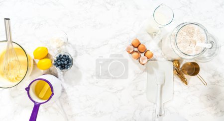 Photo for Flat lay. Integrating ingredients in a glass bowl, adeptly stirring with a whisk to craft a tantalizing lemon-blueberry bundt cake. - Royalty Free Image