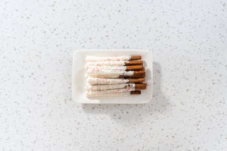 Photo for Flat lay. Pile of homemade candy cane chocolate-covered pretzel rods on a white serving plate. - Royalty Free Image