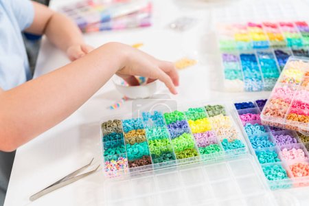 Téléchargez les photos : Petite fille aime confectionner des bracelets colorés avec des perles d'argile vibrantes ensemble. - en image libre de droit