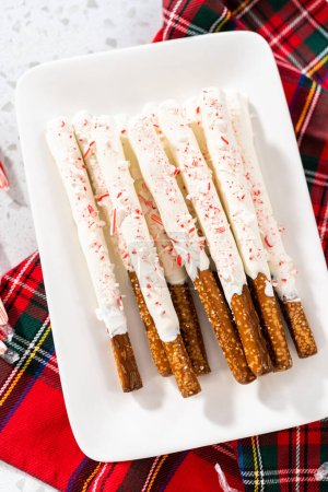 Pile of homemade candy cane chocolate-covered pretzel rods on a white serving plate.
