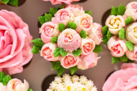 Foto de Encerrado en una caja de cupcakes de papel blanco prístino, cada cupcake gourmet es una obra de arte, adornada con flores de glaseado de crema de mantequilla bellamente diseñadas para parecerse a rosas vibrantes y tulipanes. - Imagen libre de derechos