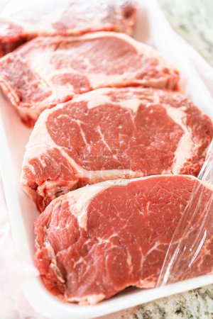 Photo for In a sleek, modern white kitchen, a high-quality rib eye steak is carefully being removed from its store packaging. The beautifully marbled steak, soon to be seasoned, promises an upcoming culinary - Royalty Free Image