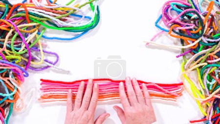 Foto de Acostado. Las manos tocan un arco iris cuidadosamente organizado de hilos de perlas de arcilla enrolladas y coloridas contra una superficie blanca contrastante. - Imagen libre de derechos