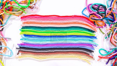 Photo for Flat lay. Hands touch a neatly organized rainbow of colorful, coiled clay bead strands against a contrasting white surface. - Royalty Free Image