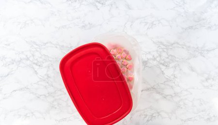 Téléchargez les photos : Pose plate. Stockage de biscuits au sucre en forme de cœur avec glaçage royal rose et blanc dans un grand récipient en plastique. - en image libre de droit