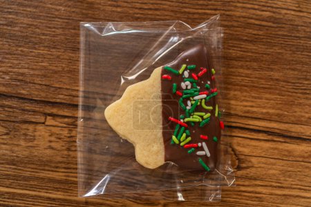 Foto de Embalaje cuidadoso galletas de recorte de Navidad, medio sumergidas en chocolate y presentadas en envoltura de celofán transparente, perfectas para regalos festivos. - Imagen libre de derechos