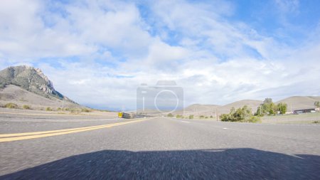 Foto de En un día de invierno crujiente, un automóvil cruza a lo largo de la icónica autopista 101 cerca de San Luis Obispo, California. El paisaje circundante es marrón y tenue, con colinas onduladas y parches de costa - Imagen libre de derechos