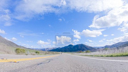 Photo for Vehicle is cruising along the Cuyama Highway under the bright sun. The surrounding landscape is illuminated by the radiant sunshine, creating a picturesque and inviting scene as the car travels - Royalty Free Image