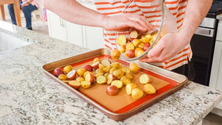 Photo for In a modern, white kitchen, a young man is engrossed in dinner preparations. His current endeavor includes arranging seasoned rainbow potatoes on a baking sheet, a meticulous step towards a - Royalty Free Image