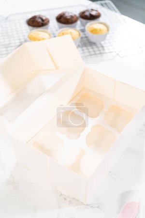 Foto de Los cupcakes de cumpleaños, bellamente adornados con decoraciones fondantes, se colocan cuidadosamente en cajas de papel blanco, listas para su gran presentación. - Imagen libre de derechos
