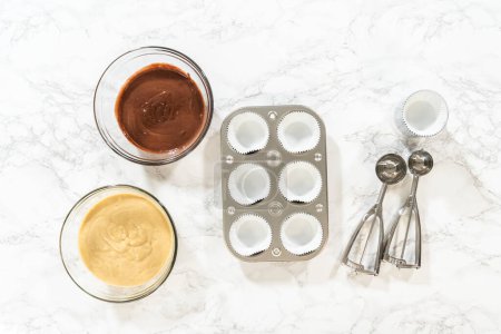 Flat lay. Cupcake foil liners are being meticulously filled with both chocolate and vanilla batter, setting the stage for the baking of deliciously diverse birthday cupcakes.