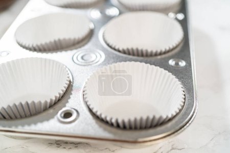 Cupcake foil liners are being meticulously filled with both chocolate and vanilla batter, setting the stage for the baking of deliciously diverse birthday cupcakes.