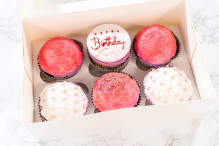 Téléchargez les photos : Les cupcakes d'anniversaire, magnifiquement décorés avec des décorations fondantes, sont soigneusement placés dans des boîtes en papier blanc, prêts pour leur grande présentation. - en image libre de droit