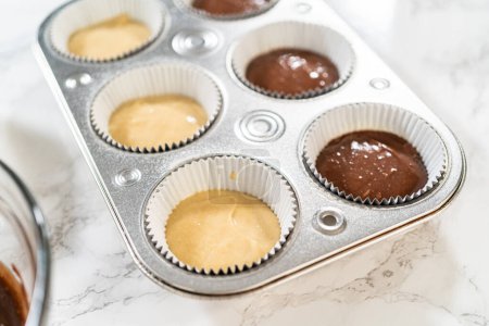 Téléchargez les photos : Les doublures en papier d'aluminium Cupcake sont méticuleusement remplies de chocolat et de pâte à la vanille, préparant le terrain pour la cuisson de cupcakes d'anniversaire délicieusement variés. - en image libre de droit