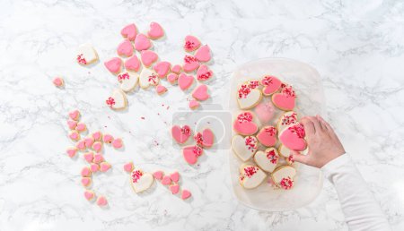 Photo for Flat lay. Storing heart-shaped sugar cookies with pink and white royal icing in a large plastic container. - Royalty Free Image