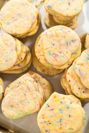 Photo for Large quantity of sprinkle-filled sugar cookies are neatly stacked on a baking tray, awaiting their packaging into the rustic brown paper boxes. - Royalty Free Image