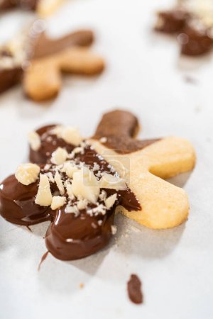 Foto de Creación de galletas de azúcar recortadas, parcialmente sumergidas en chocolate y cubiertas con trozos de avellana, colocadas en papel pergamino. - Imagen libre de derechos