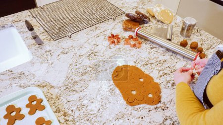 Foto de Usando varios cortadores de galletas festivas, estaban cortando encantadoras galletas de jengibre de la masa enrollada en el elegante mostrador de mármol, trayendo alegría navideña a la cocina moderna. - Imagen libre de derechos