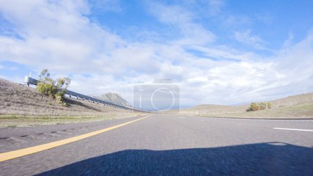 Photo for On a crisp winter day, a car cruises along the iconic Highway 101 near San Luis Obispo, California. The surrounding landscape is brownish and subdued, with rolling hills and patches of coastal - Royalty Free Image