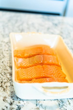 Photo for Preparing to bake fresh salmon pieces with teriyaki sauce, start by carefully arranging the raw salmon in an oven-safe ceramic baking dish. - Royalty Free Image