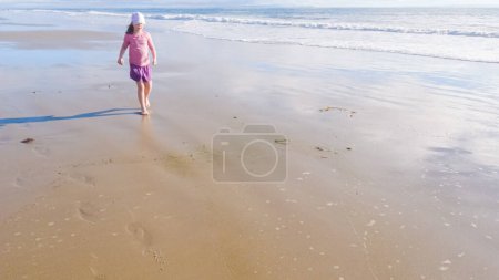Ein kleines Mädchen spielt im Winter fröhlich auf dem weiten, leeren Sand des El Capitan State Beach in Kalifornien.