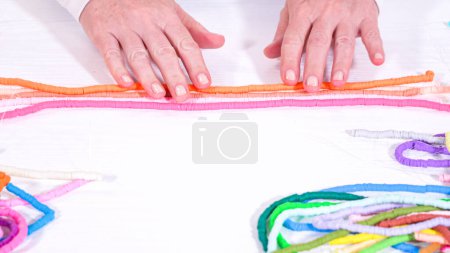 Foto de Las manos tocan un arco iris cuidadosamente organizado de hilos de perlas de arcilla enrolladas y coloridas contra una superficie blanca contrastante. - Imagen libre de derechos