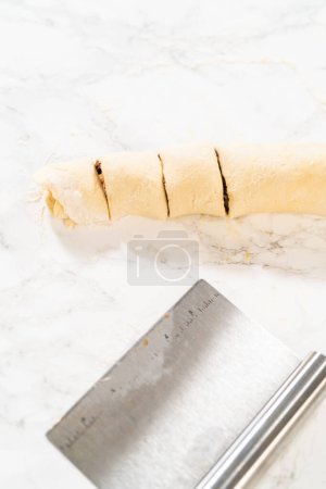 Foto de Corte de masa de pan laminado lleno de relleno de canela y pacanas picadas en rollos más pequeños para hornear pastelitos de canela sin levadura. - Imagen libre de derechos