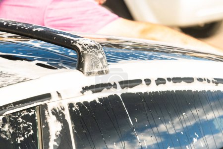 Téléchargez les photos : Nettoyage efficace d'une voiture électrique dans le confort d'une allée de banlieue, combinant éco-conscience et praticité. - en image libre de droit