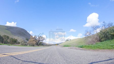Téléchargez les photos : Par une belle journée d'hiver, une voiture se déplace en douceur le long de l'autoroute 101 près de Santa Maria, en Californie, sous un ciel bleu brillant, entouré d'un mélange de verdure et de nuances dorées. - en image libre de droit