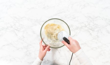 Téléchargez les photos : Pose plate. Mélanger les ingrédients dans un bol à mélanger en verre pour faire le glaçage au fromage à la crème pour les cupcakes sans levure à la cannelle. - en image libre de droit