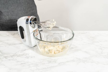 Téléchargez les photos : Mélanger les ingrédients dans un bol à mélanger en verre pour faire le glaçage au fromage à la crème pour les cupcakes sans levure à la cannelle. - en image libre de droit