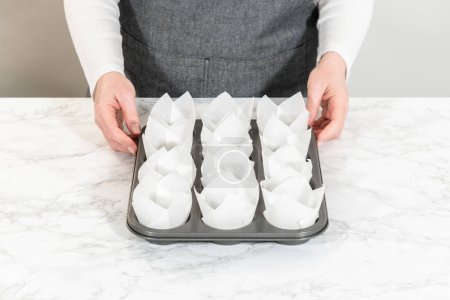 Lining baking cupcake pan with paper tulip liners to bake no-yeast cinnamon roll cupcakes.