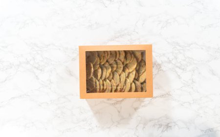Téléchargez les photos : Pose plate. Les biscuits au sucre, remplis de saupoudres mélangées dans la pâte, sont soigneusement disposés avec une précision méticuleuse dans une boîte en papier brun rustique. - en image libre de droit