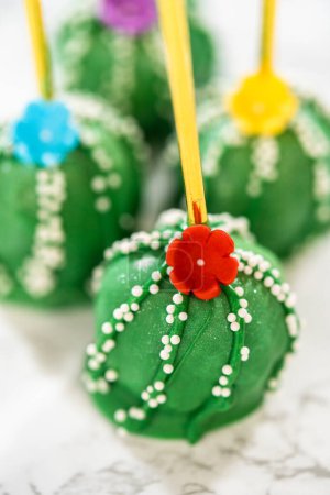 Kakteenförmige Cake Pops, wunderschön dekoriert mit Glanzstaub, Zuckerblumen und weißen Streusel, zur Feier des Cinco de Mayo arrangiert.