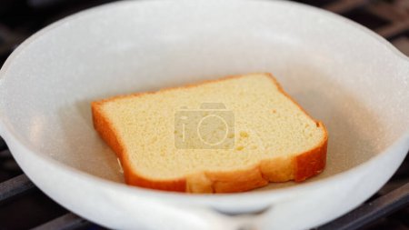 Photo for Within the sleek setting of a modern white kitchen, banana slices and brioche bread sizzle on a non-stick pan over a gas stove, setting the stage for an enticing grilled peanut butter banana sandwich. - Royalty Free Image