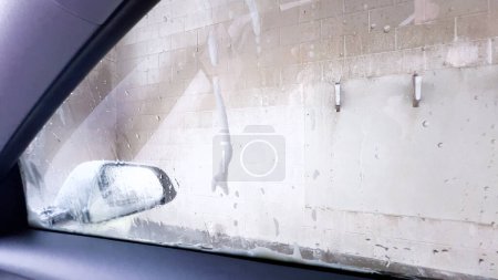 Téléchargez les photos : Vue savonneuse du pare-brise de l'intérieur d'une voiture pendant un cycle de lavage automatique, avec la mousse obscurcissant l'extérieur. - en image libre de droit