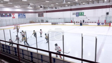 Foto de Denver, Colorado, Estados Unidos-17 de febrero de 2024-Jóvenes atletas en medio de un animado juego de hockey, con jugadores persiguiendo el disco a través de la pista de hielo bordeada por espectadores. - Imagen libre de derechos