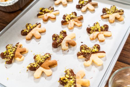 Téléchargez les photos : Fabrication de biscuits de vacances en forme d'étoile trempés dans du chocolat et saupoudrés de pistaches concassées, disposés sur du papier parchemin. - en image libre de droit