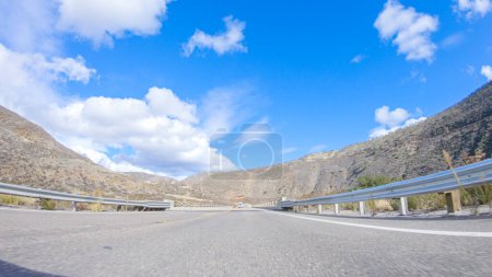 Foto de El vehículo está navegando a lo largo de la autopista Cuyama bajo el sol brillante. El paisaje circundante está iluminado por el sol radiante, creando una escena pintoresca y atractiva mientras el coche viaja - Imagen libre de derechos